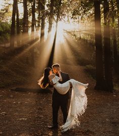 a man and woman are standing in the woods with sunlight streaming through trees behind them