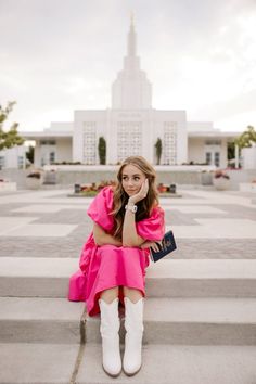 a woman sitting on the steps in front of a building wearing white boots and a pink dress