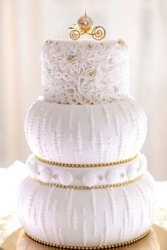 a three tiered white wedding cake with gold decorations on it's top layer