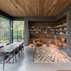 the dining room is surrounded by brick walls and floor to ceiling windows that look out onto the woods