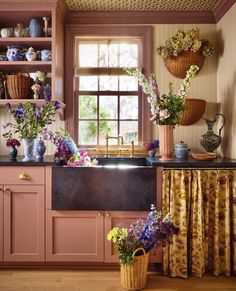 a kitchen with pink cabinets and flowers in the window sill, next to a sink