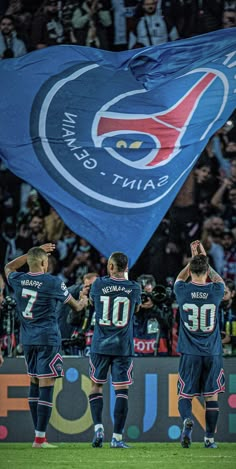 the soccer team is standing in front of a flag with their hands up to the sky