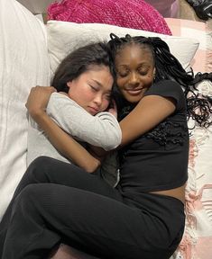 two women hugging each other while laying on a bed with white sheets and pink pillows