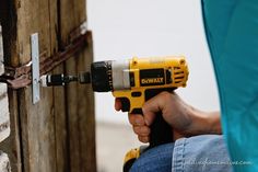 a person using a drill to fix a wooden door with nails on the outside wall