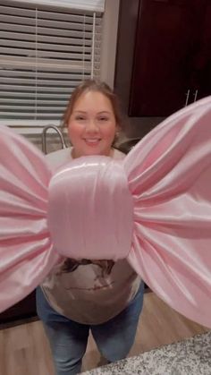 a woman holding two large pink bows in front of her face and smiling at the camera