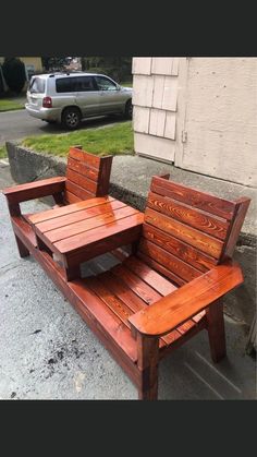 a wooden bench sitting on the side of a road next to a building and parked car