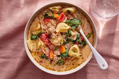 a bowl of pasta and spinach soup with a glass of water on the side