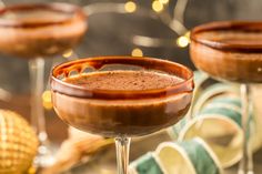 two glasses filled with chocolate drink sitting on top of a table next to christmas decorations