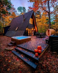 an outdoor hot tub in front of a house with fall leaves on the ground and trees surrounding it