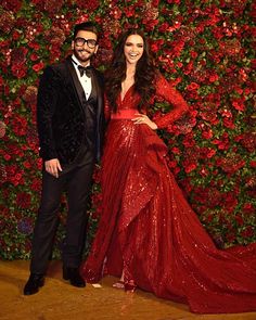 two people standing next to each other in front of a red wall with flowers on it