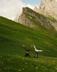 two people standing on top of a lush green hillside with mountains in the back ground