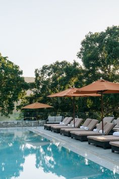 an outdoor pool with lounge chairs and umbrellas next to the swimming pool is surrounded by trees