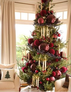 a christmas tree decorated with red and gold baubes, candles and ornaments in front of a window