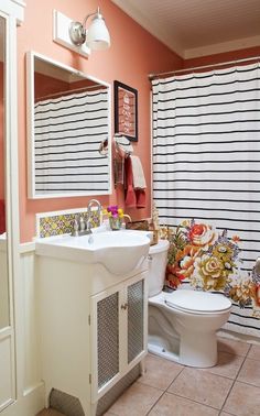 a white toilet sitting next to a sink in a bathroom under a window with striped curtains