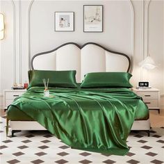 a bed with green sheets and pillows in a white room next to two pictures on the wall