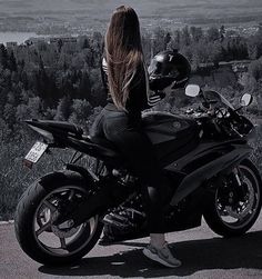 a woman sitting on top of a motorcycle looking out over the valley and trees in the distance