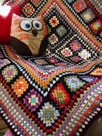 an owl sitting on top of a crocheted blanket next to a red pillow