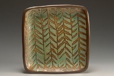 a green and brown square shaped dish with designs on the outside, sitting on a gray surface