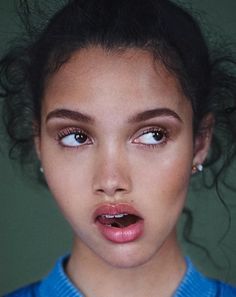 a young woman with her mouth open wearing a blue shirt and pearl earrings is looking at the camera