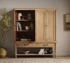 a wooden cabinet sitting in the middle of a living room next to a vase and potted plant