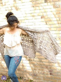 a woman is standing in front of a brick wall with her arms spread open and she has an animal print shawl over her shoulders