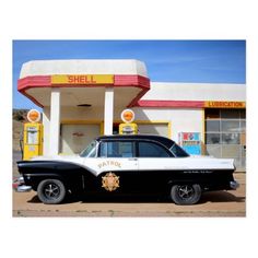 an old police car is parked in front of a shell service station with a gas pump