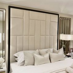 a large bed with white sheets and pillows in a bedroom next to a mirror on the wall