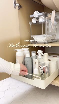 a person is holding the bottom shelf of a bathroom cabinet with soap and lotion