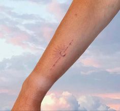 a person's arm with a sun tattoo on it and clouds in the background