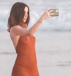 a woman in an orange dress taking a selfie on the beach