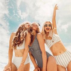 three women in bathing suits are sitting on the beach and one is holding her arms up