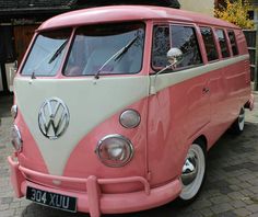 a pink and white vw bus parked in front of a building