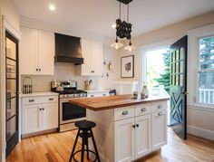 a kitchen with white cabinets and wood floors, an island in the middle is surrounded by stools