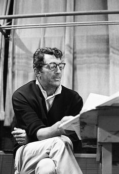 a black and white photo of a man sitting on a bench reading a paper while wearing glasses