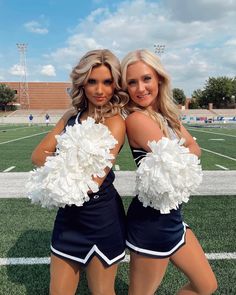 two cheerleaders posing for the camera in front of a football field with their pom poms