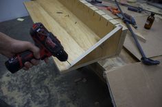 a person holding a cordless drill in front of a wooden box filled with tools