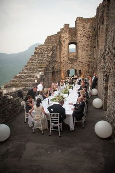 a group of people sitting around a table with white balloons in front of them on top of a stone building