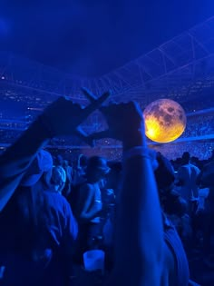 a crowd of people at a concert with their hands up in the air, and one person holding an object above his head