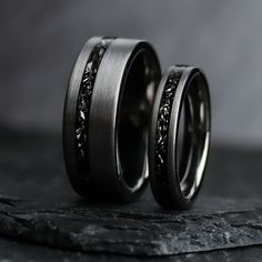 two wedding bands with black diamonds in them on top of a stone slab, against a dark background