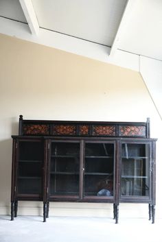 an old black china cabinet with glass doors and carvings on the front, sitting in a white room