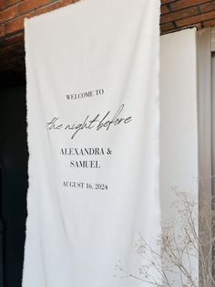 a welcome sign hanging from the side of a brick building in front of a door