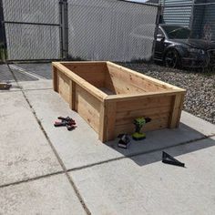 a large wooden box sitting on top of a cement floor next to a fence and some tools