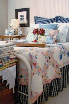 a bed covered in lots of pillows and blankets next to a table with flowers on it