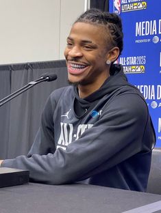 a young man sitting at a table with a microphone in front of him and smiling