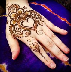 a hand with henna tattoos on it and a heart drawn on the top of it