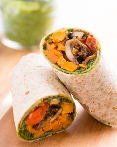 two burritos on a cutting board with a green smoothie in the background