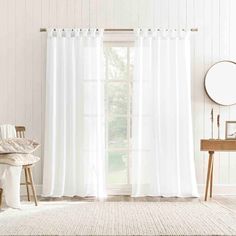 a white curtain hanging in front of a window with a mirror and chair next to it