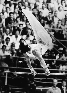 a man on a high bar in front of an audience with his legs spread out