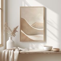 a white vase sitting on top of a wooden table next to a framed art piece