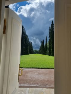 an open door leading to a lush green field with trees on the other side and clouds in the sky